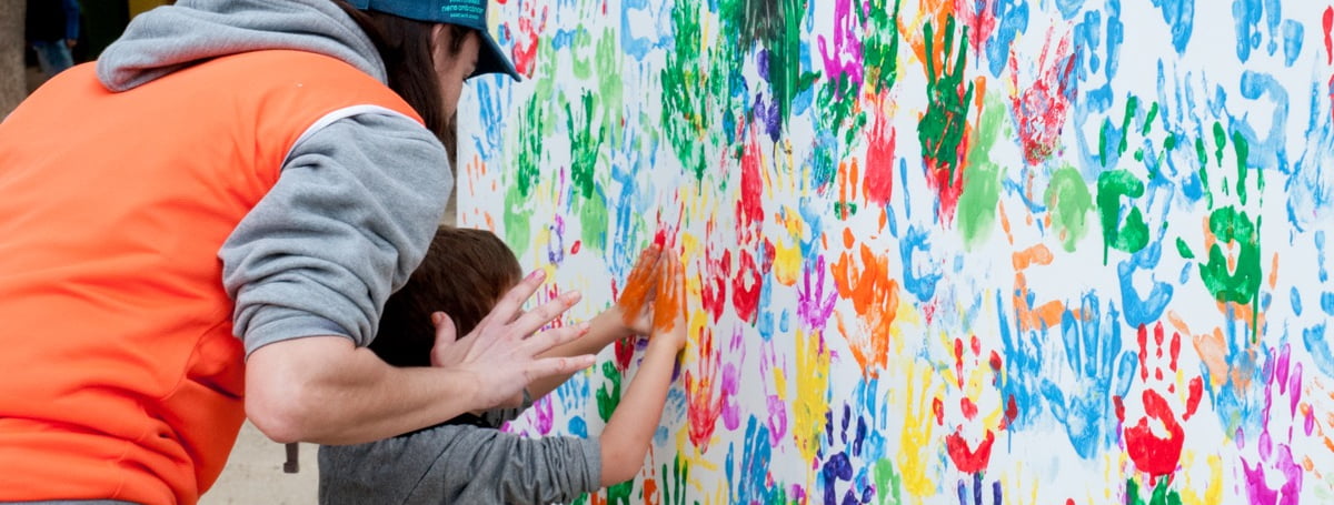 Monitora i nen fent un mural de mans amb pintura